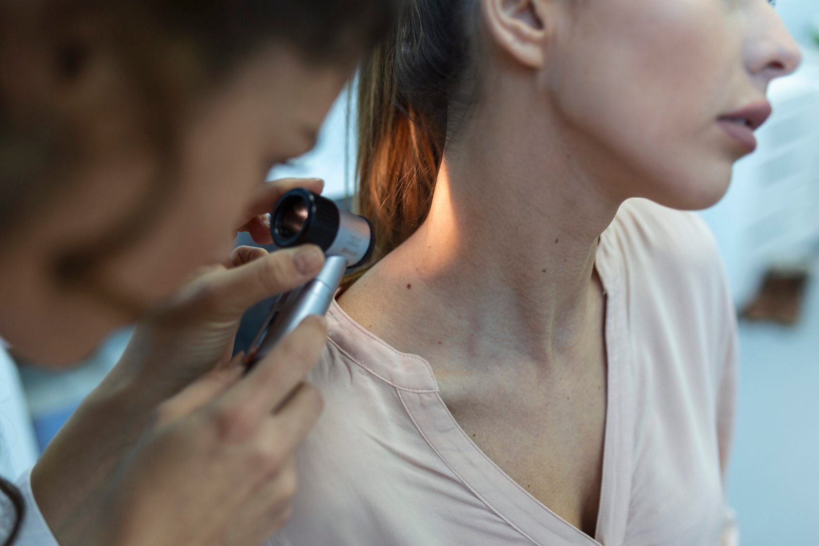 Dermatologist in latex gloves holding dermatoscope while examining attractive patient with skin disease. Female dermatologist examining patient with dermascope, looking for signs of skin cancer.